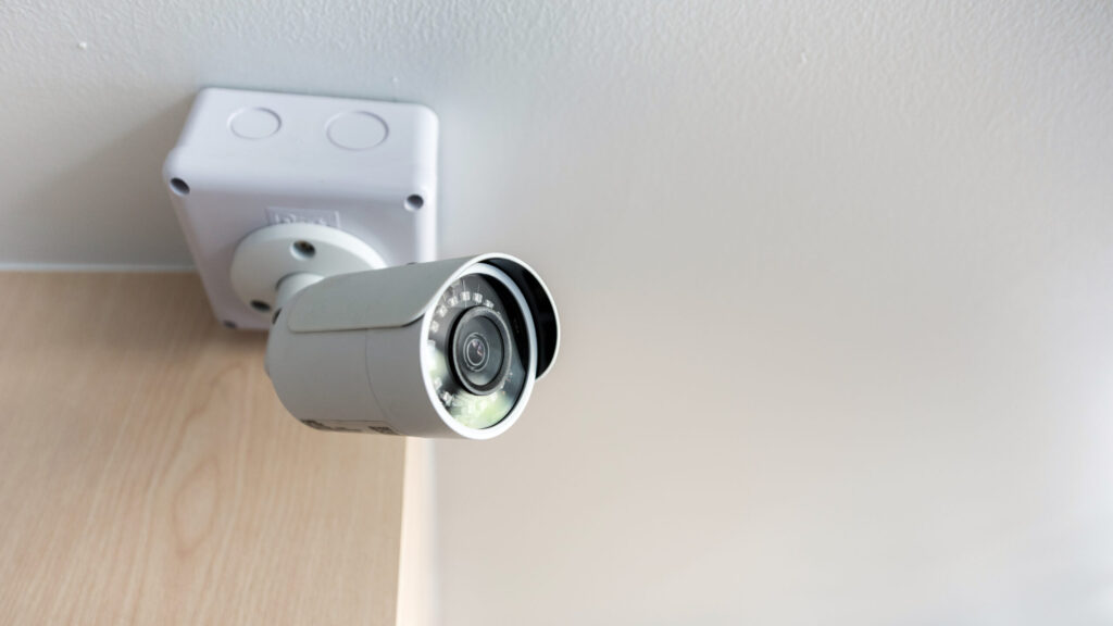 A smart camera installed on an interior ceiling by the corner of a wall.