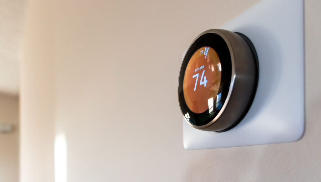 A smart thermostat mounted on an interior wall reads "In 15 min 74."